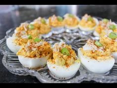 several deviled eggs are arranged on a glass platter with green onions and seasoning