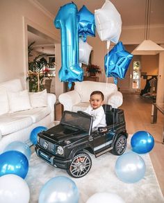 a baby is sitting in a toy jeep with blue and white balloons on the floor