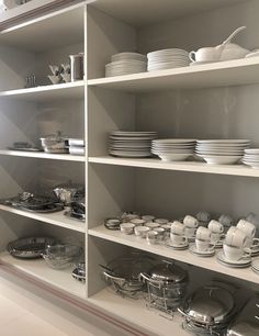 the shelves are full of dishes and plates in white, grey and silver colors on them