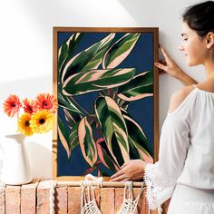 a woman standing in front of a painting with flowers on the shelf next to it