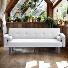 a white couch sitting in front of a window filled with potted plants and greenery