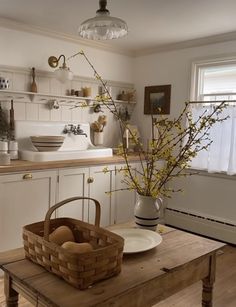 a kitchen with white cabinets and wooden table topped with a basket filled with fruit next to a sink