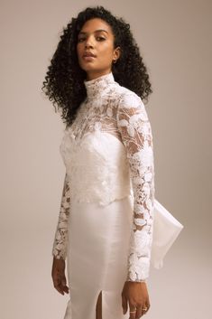 a woman wearing a white dress with sheer lace on the top and sleeves, standing in front of a gray background