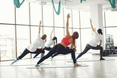 a group of women doing yoga poses in a large room with lots of windows on the wall