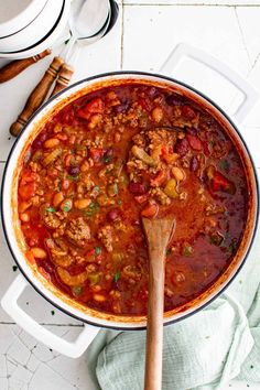 a large pot filled with chili and beans next to a wooden spoon on top of a table