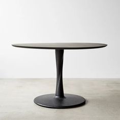 an oval table with a black base on a concrete floor in front of a white wall