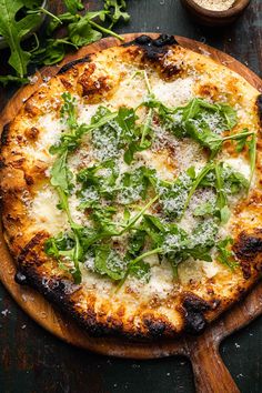 a pizza topped with cheese and greens on top of a wooden cutting board next to other ingredients