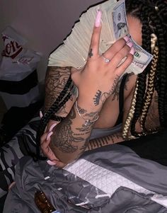 a woman with dreadlocks and tattoos on her arm holding money in one hand