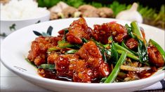 a white bowl filled with meat and vegetables on top of a table next to rice