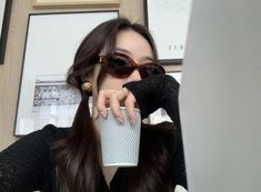 a woman wearing sunglasses and holding a cup in front of her face