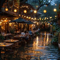 an outdoor restaurant with tables and umbrellas over the water at night, lit by lanterns