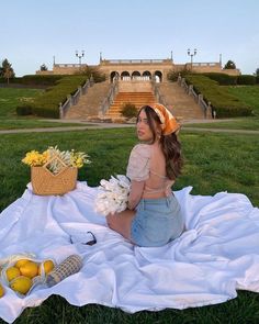 a woman sitting on top of a white blanket next to a basket of flowers and lemons