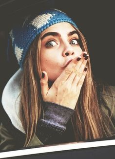 a woman wearing a blue and white knitted hat covers her mouth with her hands