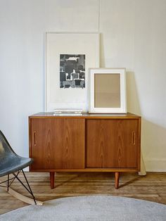 a wooden cabinet sitting next to a black chair in a living room with white walls