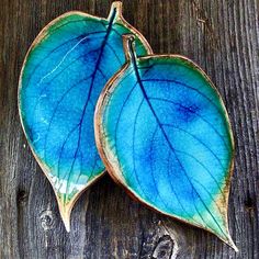 two blue and green leaf shaped dishes sitting on top of a wooden table next to each other