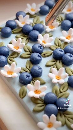 a cake with blueberries and flowers on it being cut by a pair of scissors