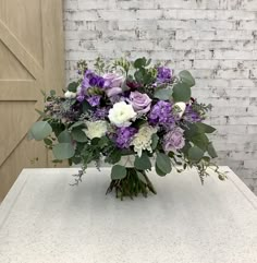 a bouquet of purple and white flowers on a table in front of a brick wall