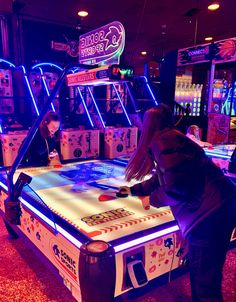 two people playing an arcade game in a room filled with neon signs and other items