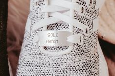 a white tennis shoe with a silver tag on the laces that says sole sisters