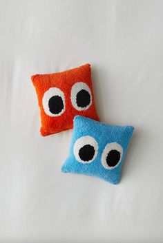 two pillows made to look like eyes are on a white surface, one is orange and the other is blue