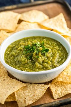 guacamole in a white bowl surrounded by tortilla chips on a tray