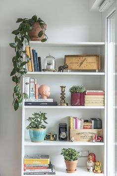 a bookshelf filled with lots of books next to a potted plant and clock