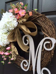 a wreath with the letter m on it and flowers hanging from it's front door