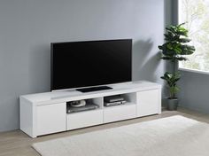 a flat screen tv sitting on top of a white entertainment center next to a potted plant