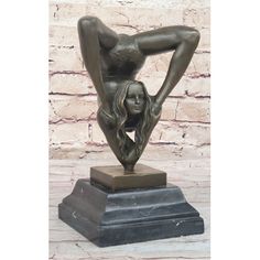 a bronze statue of a naked woman on a marble base in front of a brick wall