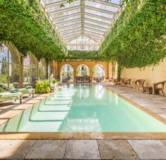 an indoor swimming pool surrounded by greenery and stone flooring, with chairs around it