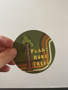 a person holding up a sticker that says plant more trees with a tree on it