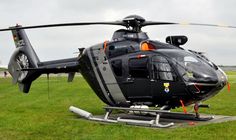 a black helicopter sitting on top of a field next to a green grass covered field