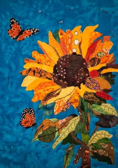 an image of a sunflower with butterflies flying around it on a blue quilted background