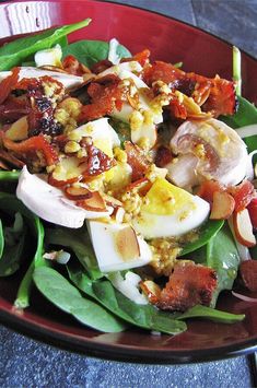 a salad with bacon, eggs and spinach leaves on a red plate sitting on a table