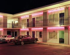 two cars parked in front of a motel at night