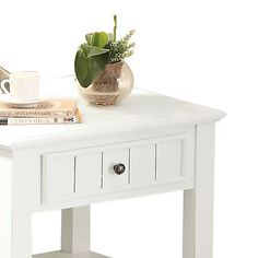 a white table with a vase and books on it, next to a coffee cup