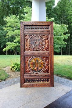 an intricately carved wooden panel on display in front of a statue with trees and grass behind it