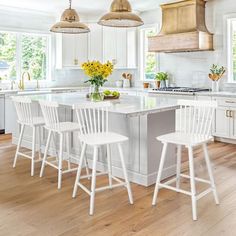 a large kitchen with white cabinets and wooden floors is pictured in this image, there are four stools at the center of the island