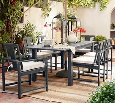 an outdoor dining table with chairs and umbrella in the middle of a patio area surrounded by potted plants