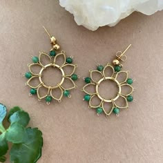 a pair of green beaded earrings sitting on top of a table next to a plant