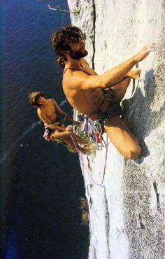 a man climbing up the side of a cliff next to another man on a surfboard