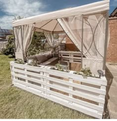 an outdoor living area with wooden pallets and white curtains on the side of it