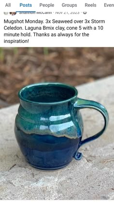 a blue mug sitting on top of a stone table next to a brick wall and grass