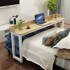 a laptop computer sitting on top of a wooden desk next to a bed with white sheets