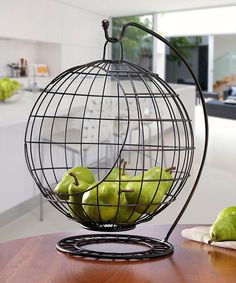 some green pears in a metal fruit bowl on a table with a kitchen in the background