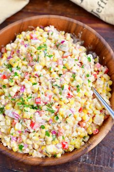 a wooden bowl filled with corn salad on top of a table