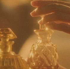 a person is holding a small glass bottle in front of a gold colored object that looks like a perfume bottle