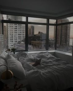 an unmade bed in front of large windows overlooking the cityscape and skyscrapers