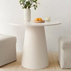 a white table with two chairs and a vase filled with oranges on the side