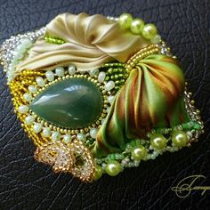 a close up of a brooch on a leather surface with pearls, beads and stones